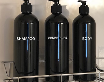 Könnte beinhalten: Drei schwarze Plastikflaschen mit Pumpen, beschriftet mit "Shampoo", "Conditioner" und "Body", auf einem silbernen Drahtgestell.