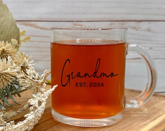 May include: A clear glass mug with a black handle. The mug has the text "Grandma Est. 2024" printed on it.