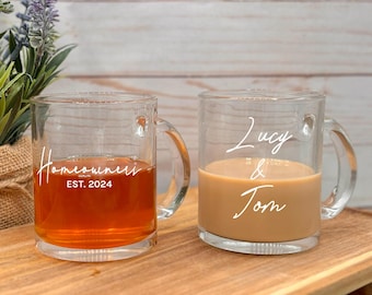 May include: Two clear glass mugs with handles. One mug has the text "Homeowners EST. 2024" and the other mug has the text "Lucy & Tom".