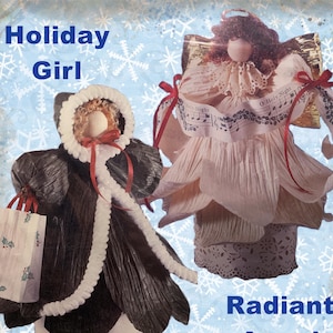 May include: Two handmade Christmas decorations: a Holiday Girl in a black coat with white trim and a shopping bag, and a Radiant Angel in a cream-colored dress with musical notes. The background is light blue with snowflakes.