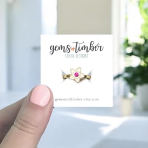 Peut inclure: Une bague dorée avec un motif en forme de fleur et une pierre rose est présentée sur une carte blanche. La carte porte le texte "gems + timber LASER DESIGNS" et l'adresse du site web "gemsandtimber.etsy.com".