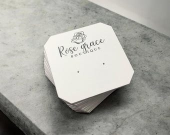 May include: A pile of white earring display cards, each with a geometric shape and two small holes. The cards are printed with the text "Rose grace BOUTIQUE" and a rose graphic in black.