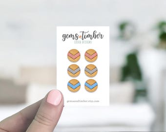 May include: A card displaying six wooden stud earrings. Each earring features a circular wooden base with a chevron design in pink, grey, and blue. The card is branded with "gems+timber LASER DESIGNS" and a website address.