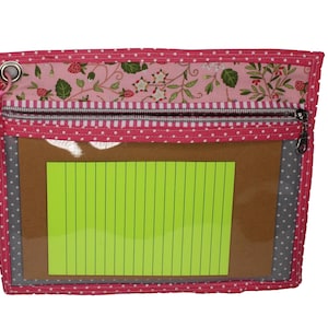 May include: A rectangular zippered pouch featuring a pink fabric with white polka dots, a top panel with a strawberry and vine print, and a clear vinyl front window. A bright neon green lined notepad is visible inside the clear pocket section.