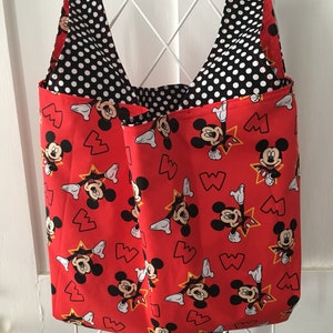 May include: Red reusable shopping tote bag with a black and white polka dot lining. The bag features a repeating pattern of Mickey Mouse with yellow stars and red hearts.