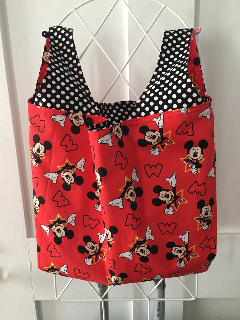 May include: Red reusable shopping tote bag with a black and white polka dot lining. The bag features a repeating pattern of Mickey Mouse with yellow stars and red hearts.
