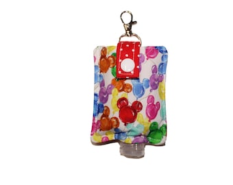 Könnte beinhalten: Ein weißer Stoff-Handdesinfektionsmittel-Halter mit einem roten Tupfenband und einem silbernen Schlüsselanhänger. Der Halter zeigt einen bunten Druck von Mickey Mouse-Ballons.