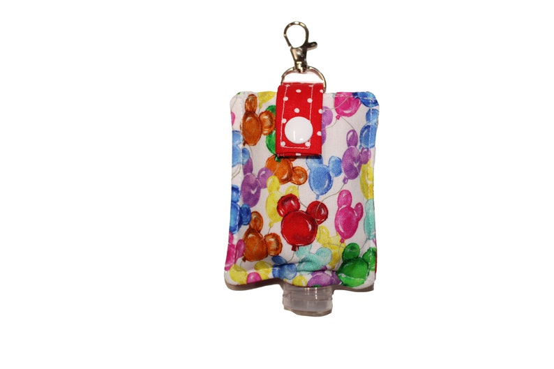 May include: A white fabric hand sanitizer holder with a red polka dot strap and a silver keychain. The holder features a colorful print of Mickey Mouse balloons.