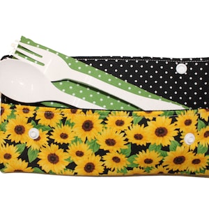 May include: A white reusable utensil set with a spoon and fork, inside a black and white polka dot fabric pouch with a sunflower print.