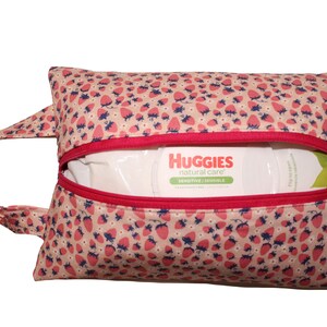 May include: A pink and white fabric zippered pouch with a strawberry print. The pouch has a red zipper and a handle. The pouch is open and contains a package of Huggies natural care baby wipes.