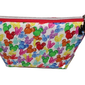 May include: A white zippered pouch with a red zipper and a black castle charm. The pouch is covered in a pattern of colorful Mickey Mouse balloons.