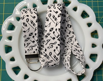May include: Two white fabric lanyards with black musical notes and symbols. The lanyards are on a white plate with a scalloped edge.