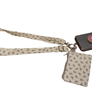 Puede incluir: Una correa de teléfono beige con un patrón de abejas, una pequeña bolsa beige con un patrón de abejas y una funda de teléfono negra con un agarre de teléfono de donut rosa.