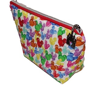 May include: A white zippered pouch with a red zipper and a silver charm. The pouch is covered in a colorful pattern of Mickey Mouse heads shaped like balloons.