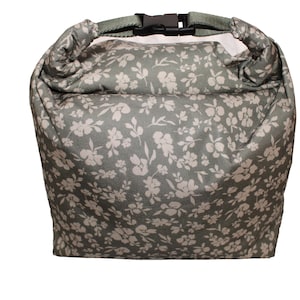 Puede incluir: Una bolsa de almuerzo verde con un estampado floral blanco. La bolsa tiene una correa negra con una hebilla.