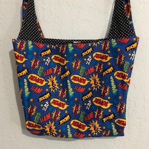 以下が含まれることがあります： 黒のストラップと「ズーム」「スラム」「パウ！」「スーパー！」などの言葉が書かれたコミック柄の青いトートバッグ。バッグの内側は白のドット柄の黒い生地で裏打ちされています。