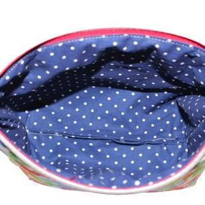 May include: A red zippered pouch with a white polka dot lining. The pouch is made of a colorful fabric with a floral pattern.