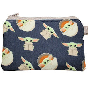 May include: A small blue zippered pouch with a repeating pattern of a green alien character. The pouch has a silver zipper and a silver ring attached to the side.