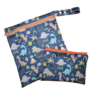 May include: Two zippered bags with a dinosaur print. The larger bag has a handle and the smaller bag is a flat pouch. Both bags have a blue background with orange zippers and a variety of colorful dinosaurs, including green, brown, and blue. The text "ROAR" appears on both bags.
