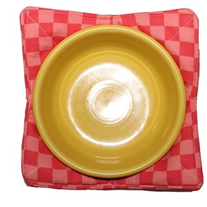 May include: A yellow ceramic bowl sits on a red and white checkered fabric hot pad.