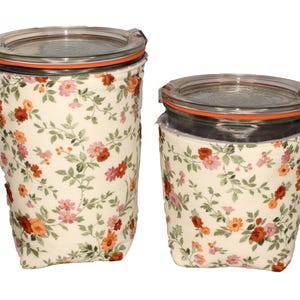 May include: Two glass storage jars with clear lids and orange rubber seals, each encased in a cream-coloured fabric sleeve featuring a repeating floral pattern of small red, orange, and pink flowers with green leaves and stems.
