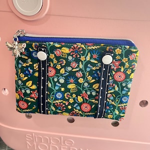 May include: A green and floral zippered pouch with blue trim and white buttons. The pouch is attached to a pink tote bag with the text "simple MODERN" on the bottom.