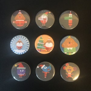 Peut inclure: Neuf badges de Noël en forme de bouton représentant des personnages de la série télévisée pour enfants 'Les Octonautes'. Les personnages portent des bonnets de Père Noël et des vêtements de fête. Les badges sont ronds et ont un fond blanc avec un contour noir.