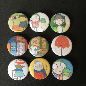 Peut inclure: Neuf boutons ronds colorés avec différentes illustrations. Les boutons représentent des personnages d'un livre pour enfants, dont un flamant rose, une fille avec un canard, une fille avec un parapluie, un boulanger, une fille avec un chat et une fille avec un chien.