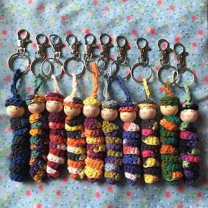 May include: Ten colorful crocheted doll keychains with wooden heads and painted faces. Each keychain has a silver metal key ring.