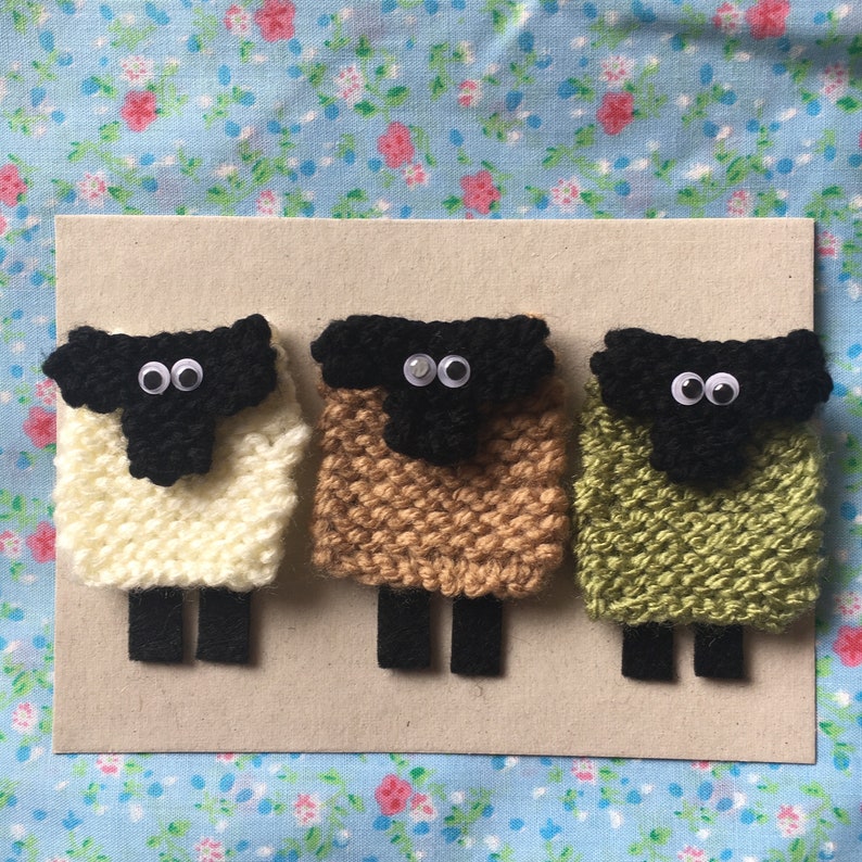 May include: Three knitted sheep ornaments, each with a black face and white eyes. The sheep are white, brown, and green.