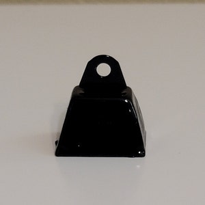May include: A small, black metal bell with a square base and a loop at the top.