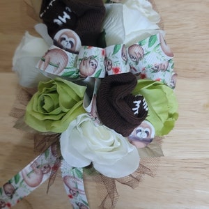 May include: A bouquet of white and green roses with brown socks and sloth-themed ribbon. The socks have a white inscription on them.