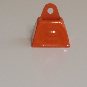 May include: A small, orange metal bell with a loop at the top. The bell is approximately 2.5 cm in diameter.
