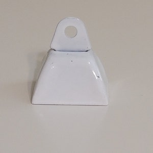 May include: A small white metal bell with a loop on top. The bell is approximately 2.5 cm tall and 2.5 cm wide.