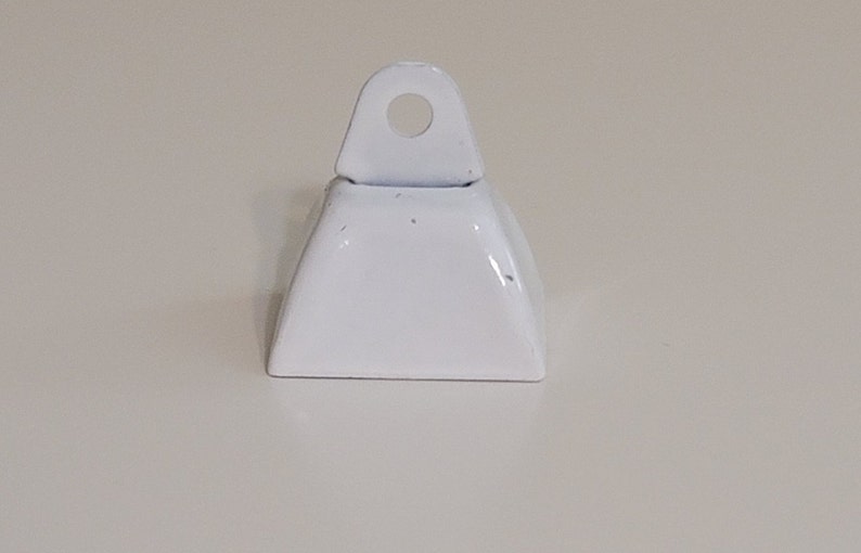 May include: A small white metal bell with a loop on top. The bell is approximately 2.5 cm tall and 2.5 cm wide.
