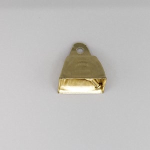 May include: A small, gold-coloured bell with a rounded top and a small, round hole at the top. The bell has a slightly textured surface and a small, silver-coloured clapper.