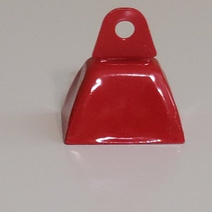 May include: A red metal cowbell with a loop handle. The bell is a traditional shape with a rounded top and a flat base.