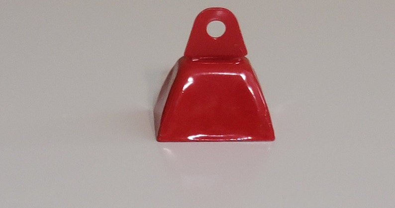 May include: A red metal cowbell with a loop handle. The bell is a traditional shape with a rounded top and a flat base.