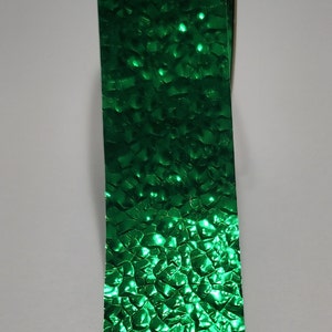 May include: A roll of emerald green ribbon with a textured, faceted surface. The ribbon's surface reflects light, creating a sparkling effect. The ribbon is likely used for gift wrapping or crafting.