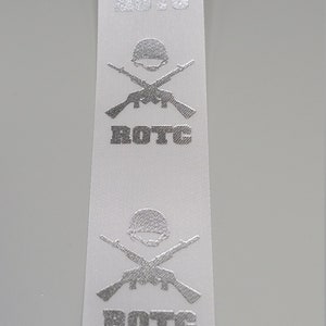 May include: White ribbon with a silver embossed design of crossed rifles and a helmet with the word "ROTC" repeated four times.