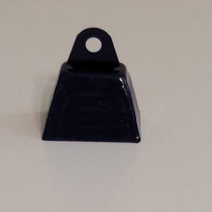 May include: A black metal cowbell with a loop at the top. The bell is approximately 5 cm tall and 5 cm wide.