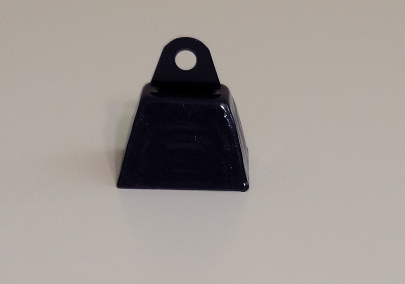 May include: A black metal cowbell with a loop at the top. The bell is approximately 5 cm tall and 5 cm wide.