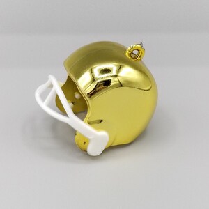 Peut inclure: Une d&eacute;coration de casque de football am&eacute;ricain dor&eacute;e avec une visi&egrave;re blanche. Le casque a une finition brillante et m&eacute;tallique et une boucle sur le dessus pour l'accrocher.