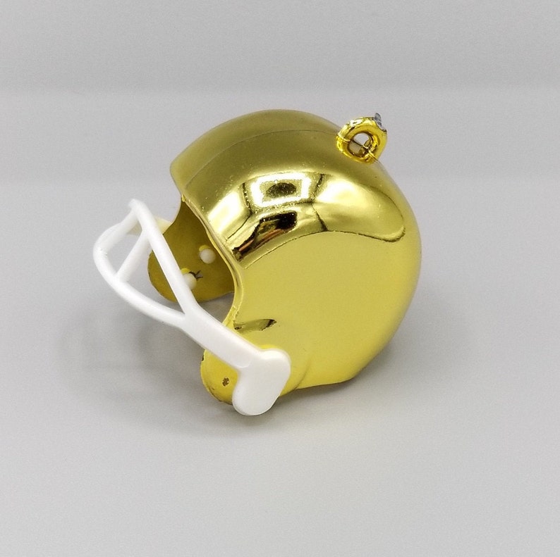 Peut inclure: Une d&eacute;coration de casque de football am&eacute;ricain dor&eacute;e avec une visi&egrave;re blanche. Le casque a une finition brillante et m&eacute;tallique et une boucle sur le dessus pour l'accrocher.