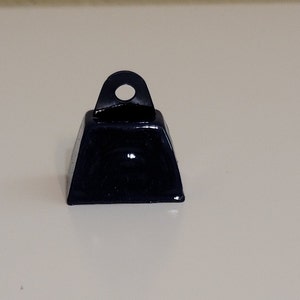 May include: A small, black metal bell with a rounded top and a loop for hanging. The bell has a smooth, shiny finish.