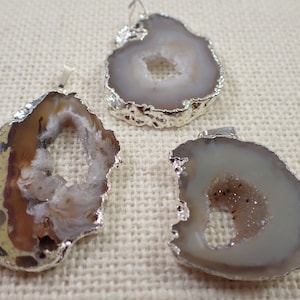 May include: Three agate slice pendants with silver-toned metal settings. The agate slices are translucent and have a white, brown, and gray color pattern. The pendants are perfect for jewelry making.