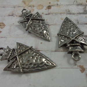 Könnte beinhalten: Drei silberne Pfeilspitzen-Anhänger mit einer strukturierten Oberfläche und einem Seil-Design. Die Anhänger haben eine Öse oben zum Anbringen an Schmuck.