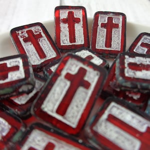 May include: A pile of red glass tiles with white crosses. The tiles are rectangular and have a slightly textured surface.