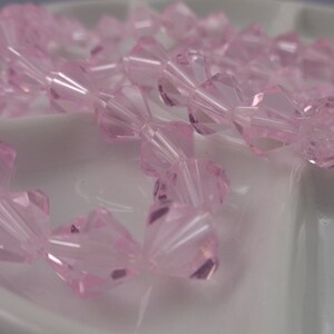 Puede incluir: Una hebra de cuentas de vidrio facetadas de color rosa. Las cuentas tienen forma de peque&ntilde;os conos y tienen una apariencia clara y transl&uacute;cida.
