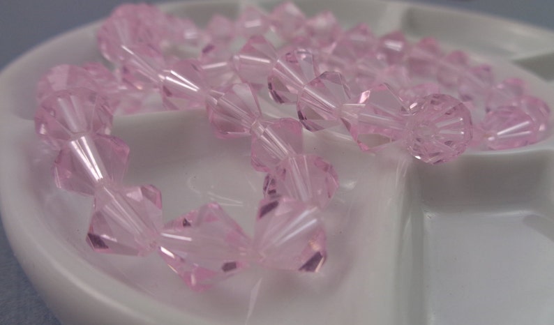 Puede incluir: Una hebra de cuentas de vidrio facetadas de color rosa. Las cuentas tienen forma de peque&ntilde;os conos y tienen una apariencia clara y transl&uacute;cida.